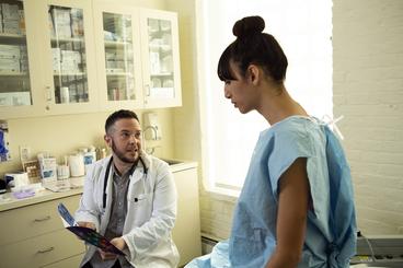 A transgender woman in a hospital gown speaking to her doctor, a transgender man, in an exam room. Image by Zackary Drucker for the Gender Spectrum Collection